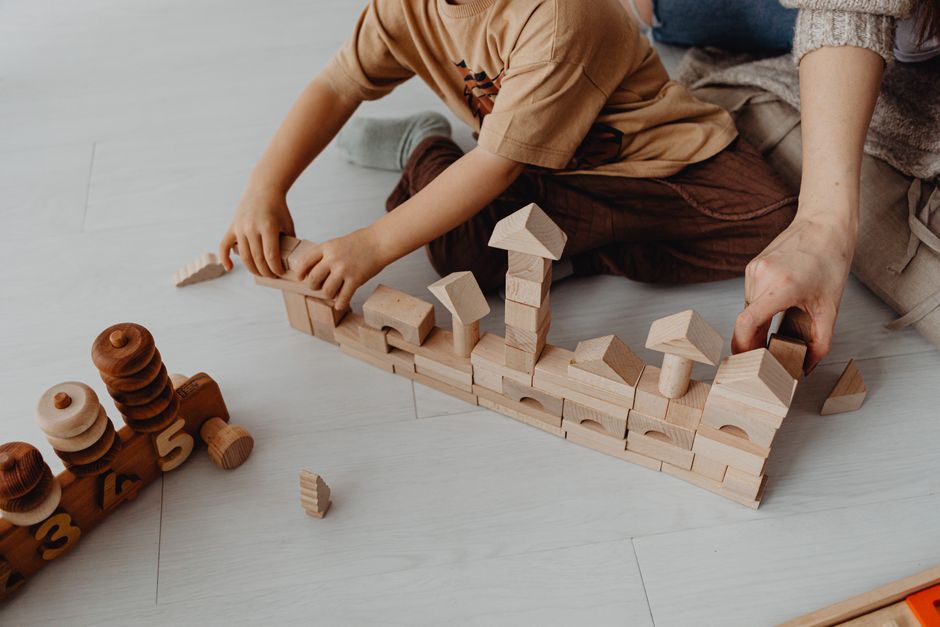 A child and an adult assembling wooden blocks on a light floor, encouraging creativity and learning.