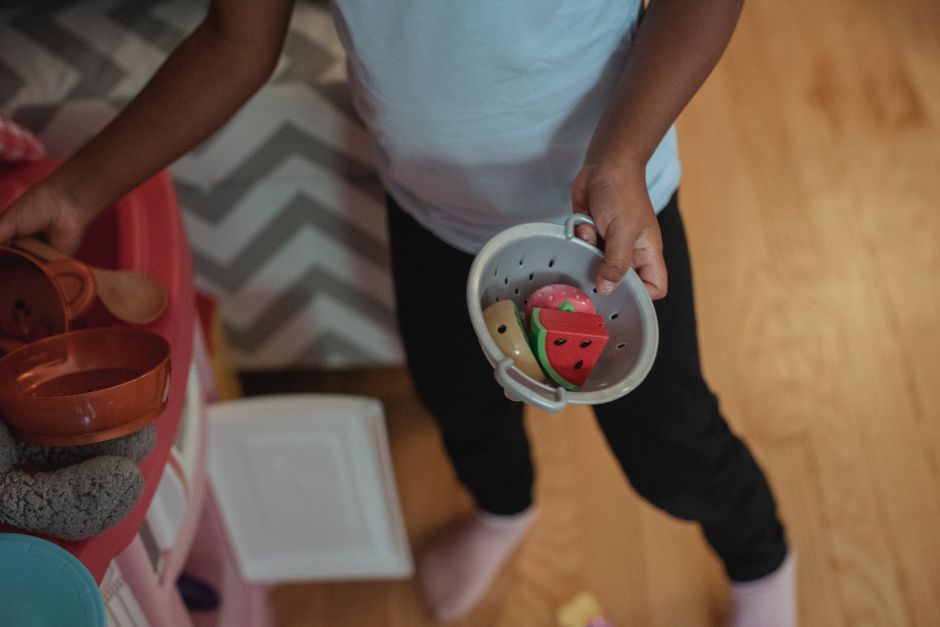 Crop faceless ethnic child using plastic kitchenware while playing on small toy kitchen at home