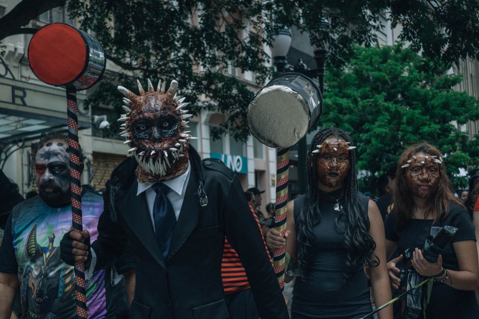 Group in elaborate monster costumes with large hammers, outdoors in urban parade setting.