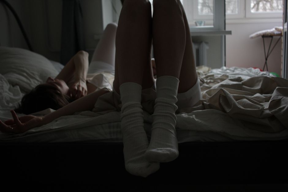 A person relaxes in bed wearing socks, creating a moody and intimate atmosphere.