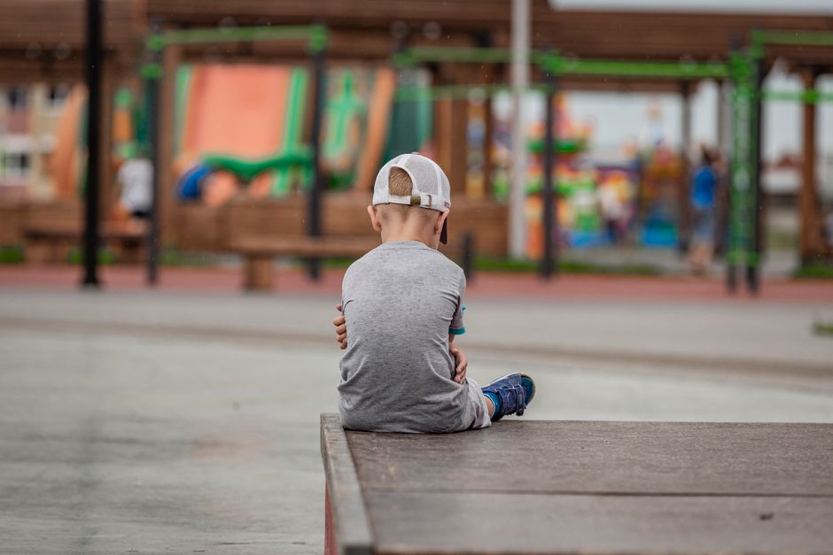 A young boy sits alone on the edge of a playground in contemplation.