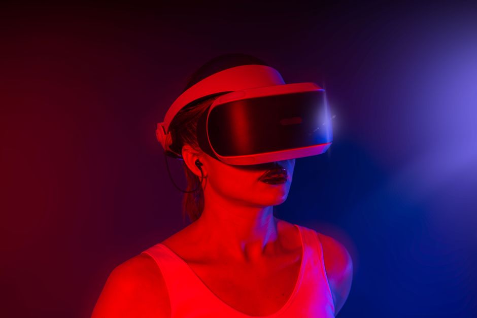 A young woman wearing a VR headset, immersed in virtual reality with red and blue lighting.