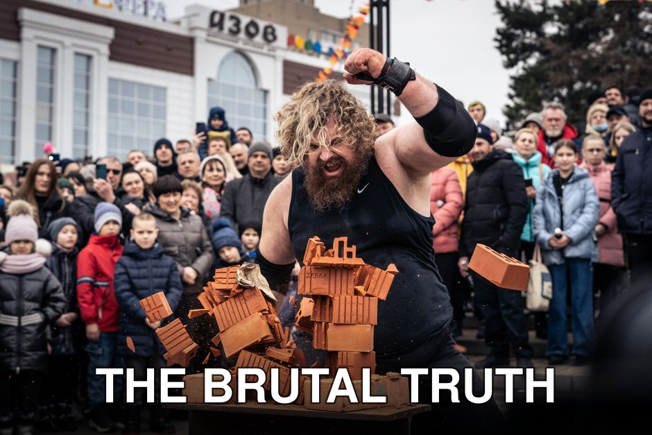 A strongman showcases strength by breaking bricks in front of a captivated crowd outdoors.