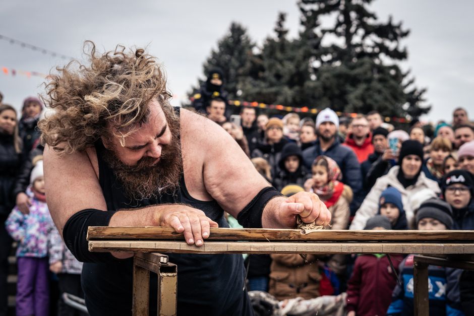 A strongman showcasing his strength at an outdoor event with a captivated crowd watching.