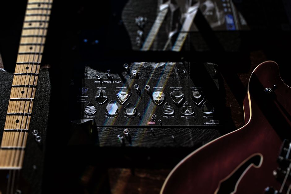 A collection of guitar picks displayed under electric guitars with dramatic lighting and shadows.