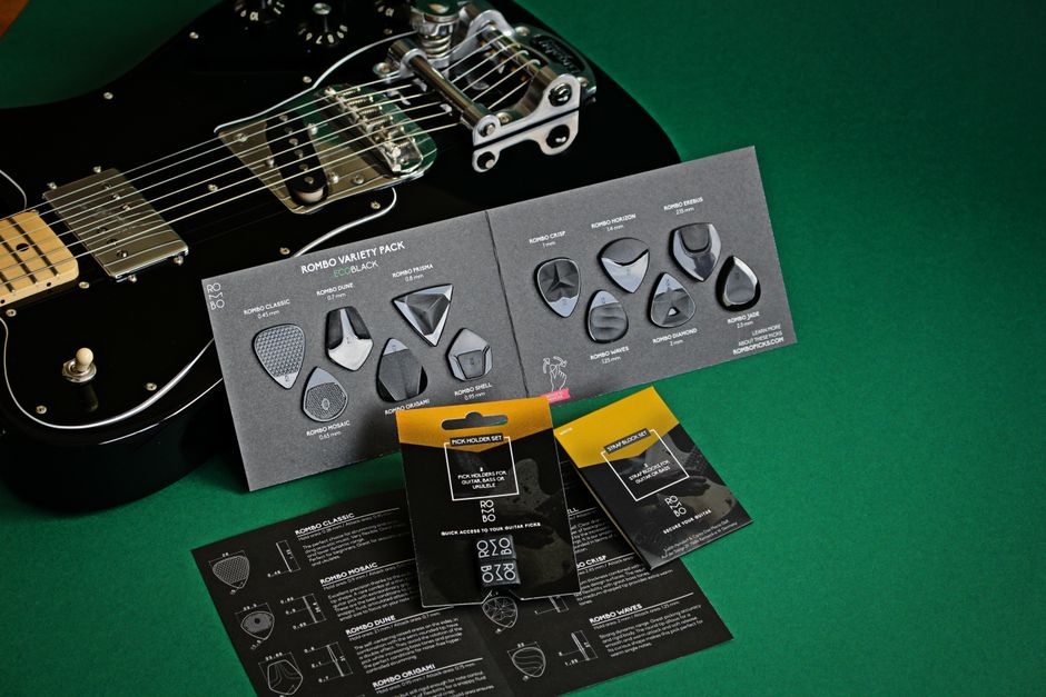 Black electric guitar with variety of guitar picks on a green background.