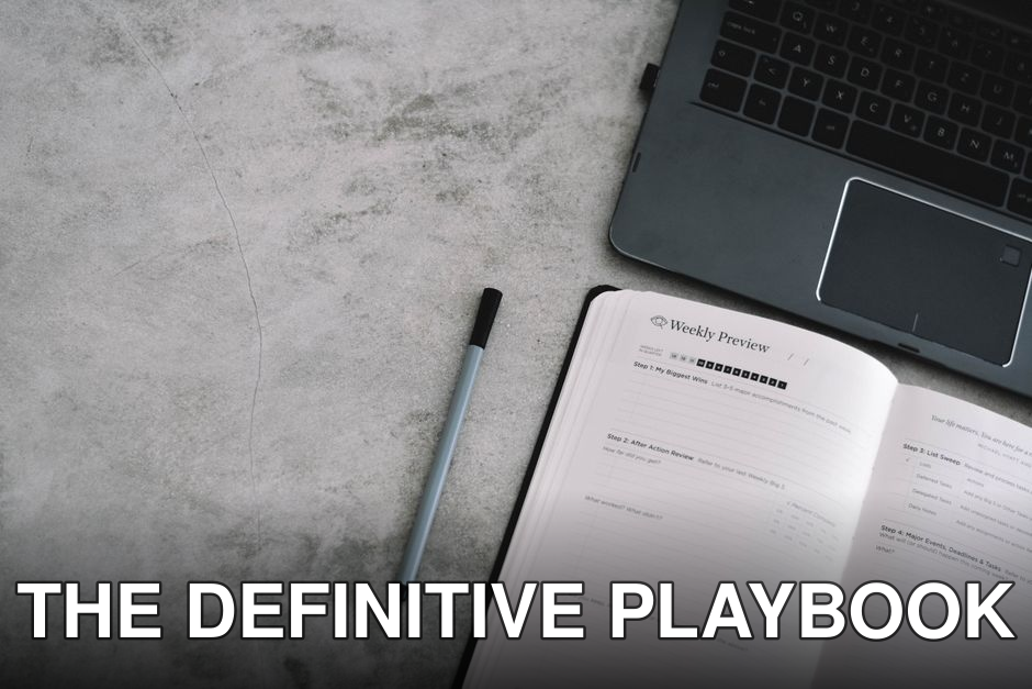 A top view of a minimalist workspace with a planner, pen, and laptop on a gray surface.