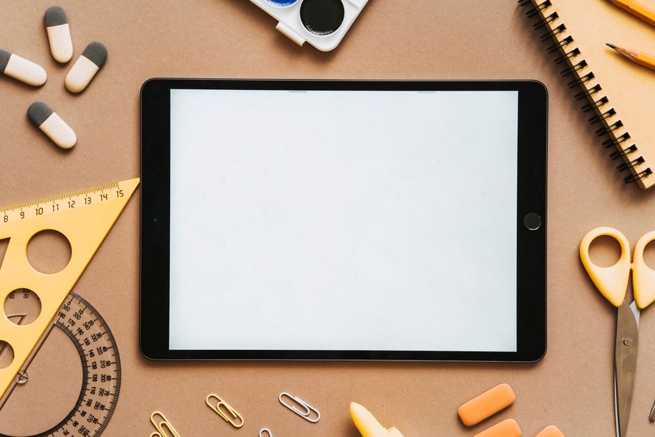 A flat lay featuring a tablet surrounded by school stationery items on a brown background.