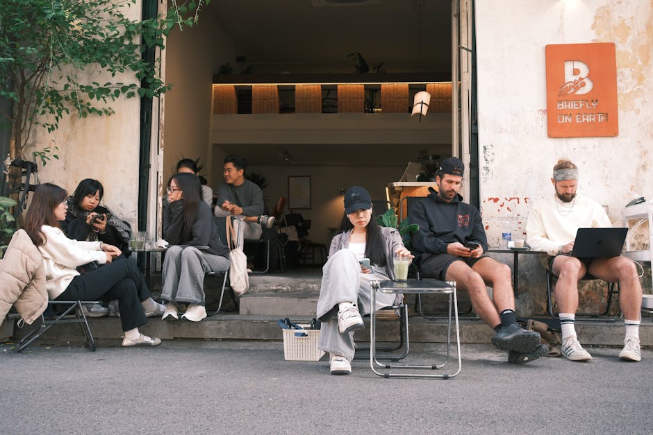 Young adults relaxing and socializing outside a cafe, enjoying drinks and conversations on a sunny day.