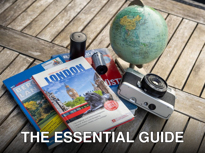 A vintage travel setup with guidebooks, a globe, and a film camera on a wooden table.