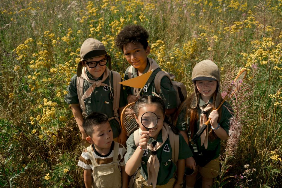 Group of children dressed as scouts exploring a wildflower meadow in summer.