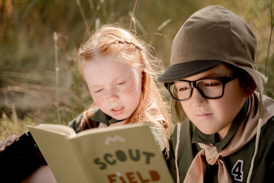 Two young scouts reading a field guide outdoors, showcasing teamwork and learning.
