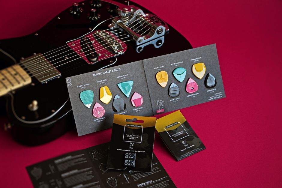 Vibrant still life of Rombo guitar picks variety pack and electric guitar on a red backdrop.