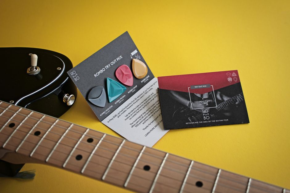 Selection of colorful guitar picks with electric guitar on a vibrant yellow surface.
