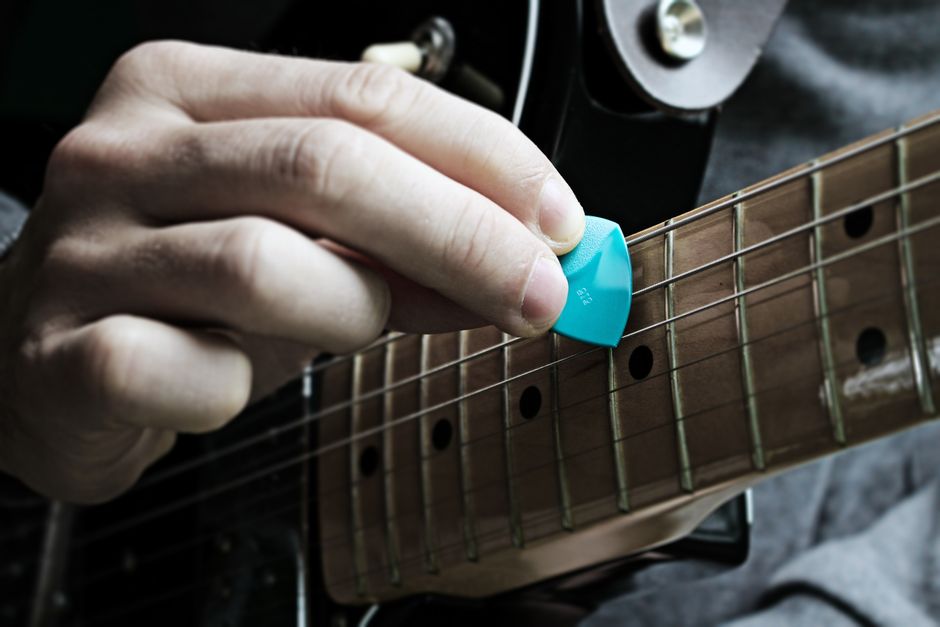 Detailed view of a hand strumming an electric guitar using a blue guitar pick.