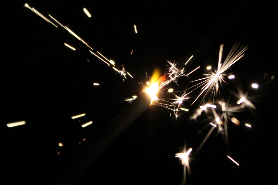 A close-up of a sparkler emitting bright sparks against a dark background, ideal for festive themes.