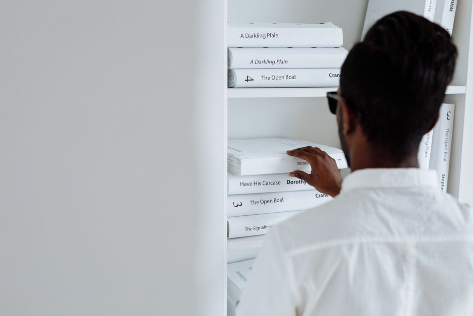 Adult browsing books on a minimalist white shelf, focusing on modern design.