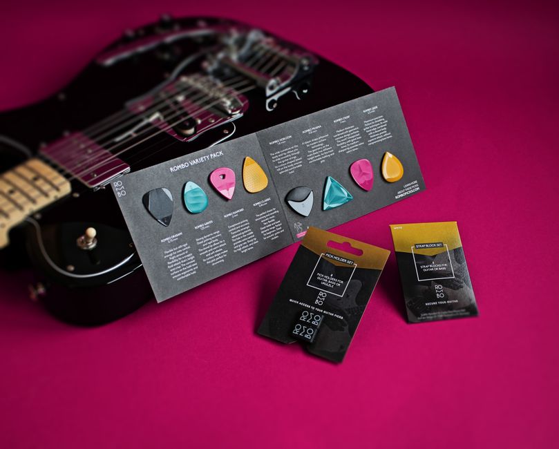 Close-up of a variety pack of colorful guitar picks beside a black electric guitar.