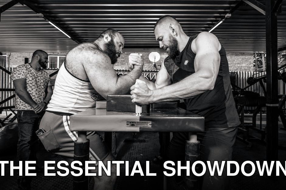Two muscular men engaged in an arm wrestling match indoors, showcasing strength and competition.