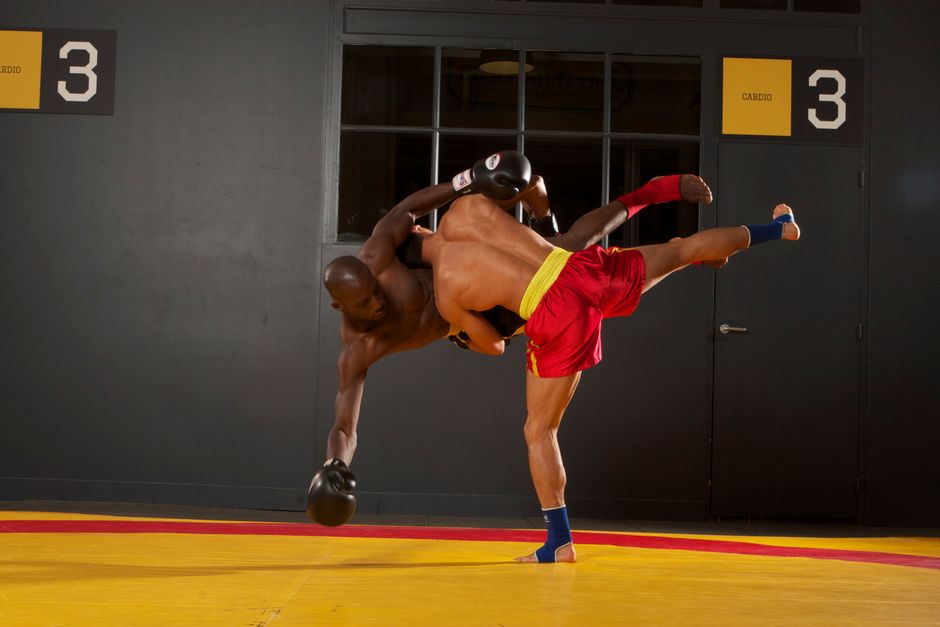 Two athletes sparring in an intense mixed martial arts training session indoors.