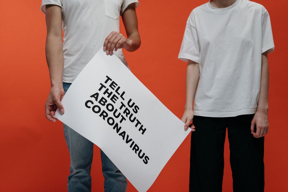 Two people holding a sign about coronavirus truth against an orange backdrop.