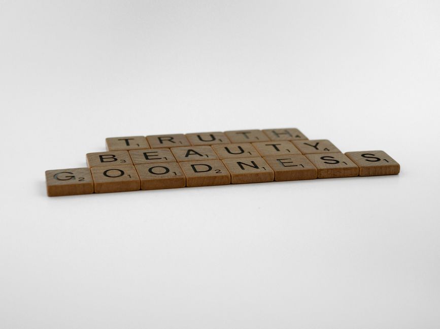 Wooden Scrabble tiles spelling truth, beauty, and goodness on a white background.