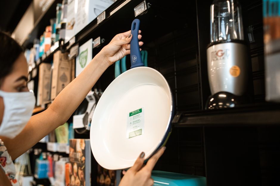 A woman in a mask shops for a frying pan at a store, a common pandemic scenario.