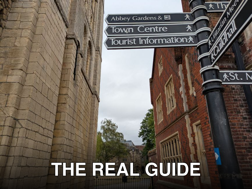 Directional signpost in a historical town center near Abbey Gardens.