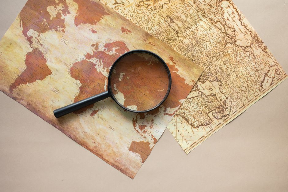 Top view of round black magnifying glass placed on paper maps with continents on beige background in light modern room