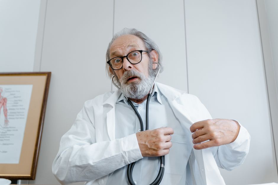 Surprised elderly doctor wearing lab coat and stethoscope indoors.