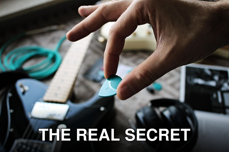 Hand holding a turquoise guitar pick above an electric guitar with accessories. Musical scene.