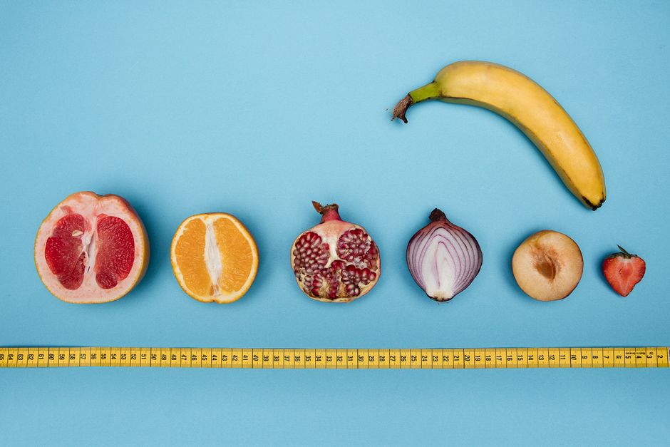 Fruits arranged with a measuring tape on a blue surface, symbolizing size and sexuality.