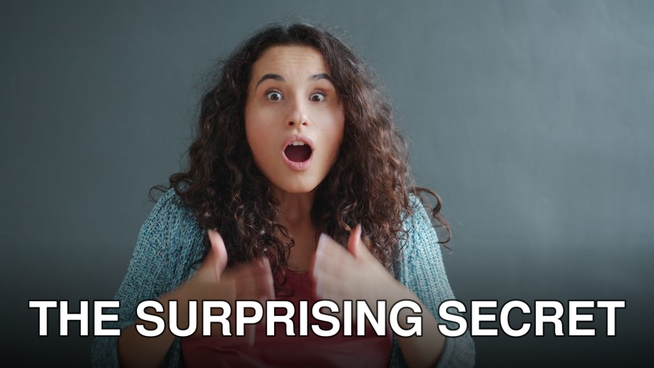 A surprised woman expressing emotion indoors with a gray background.