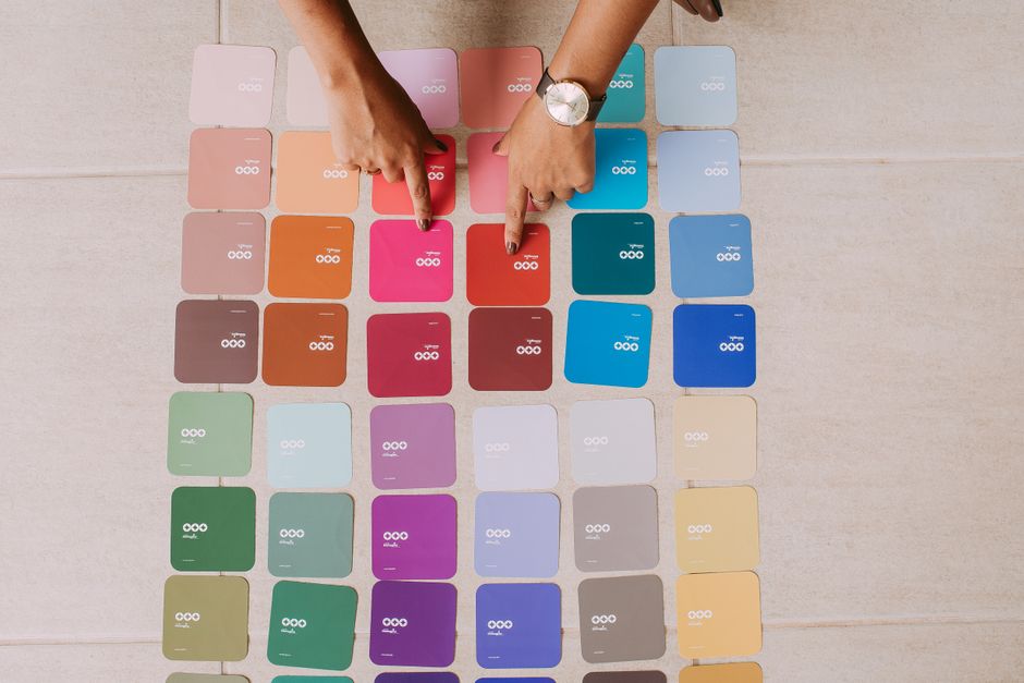 Top view of hands pointing at various color palette cards on a table, showcasing diverse options.