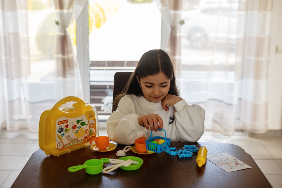 A young girl engaged with a colorful toy kitchen set indoors, perfect for imaginative play.