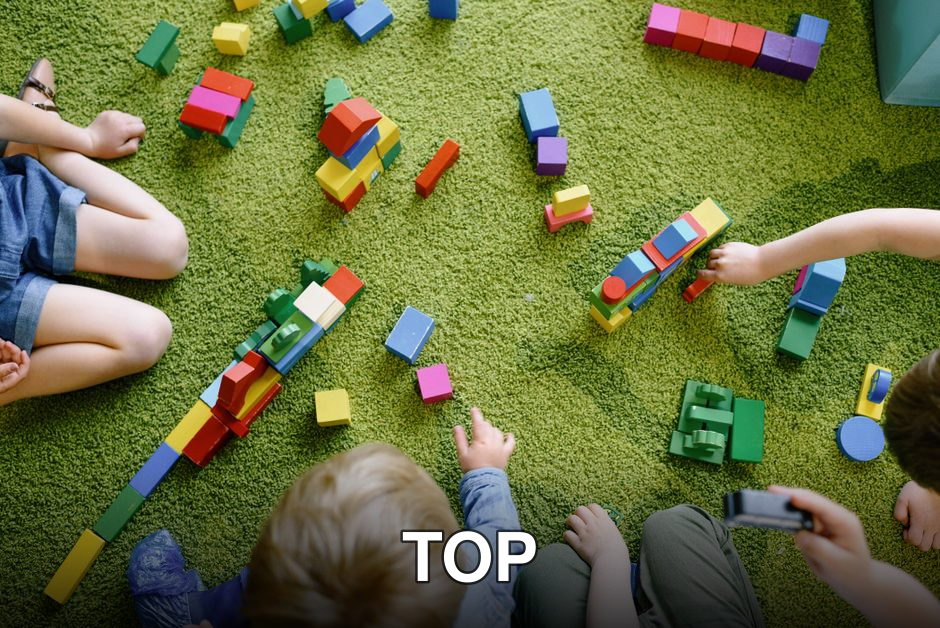 Children playing with wooden blocks on a green carpet in a classroom setting.
