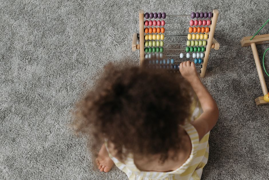 A young girl engaging with a colorful wooden abacus on a carpet, showcasing playful learning.