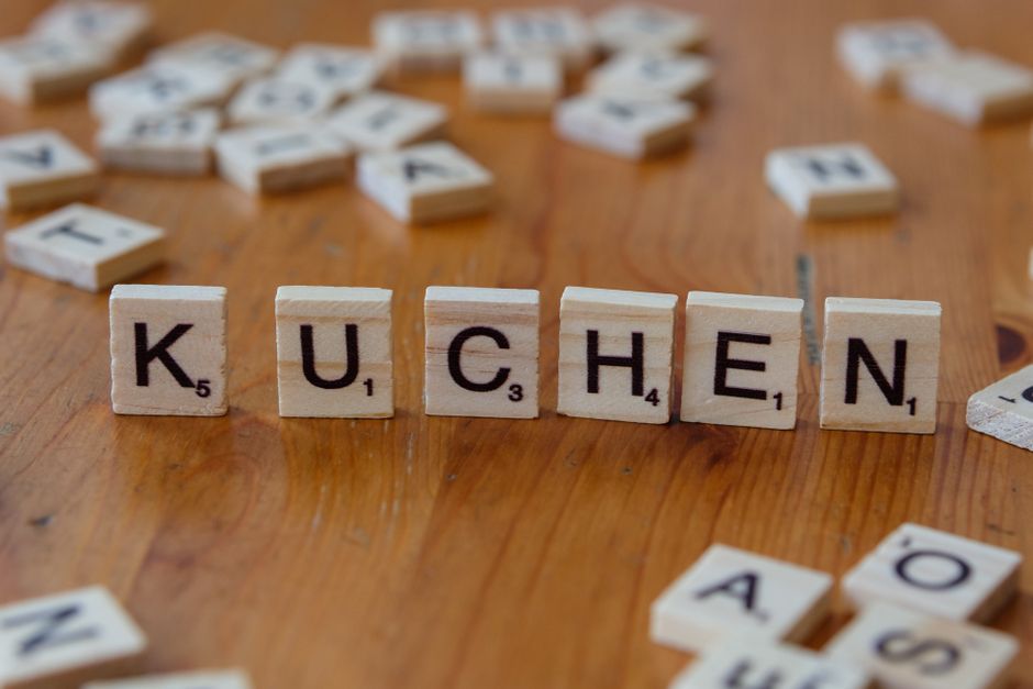 Scrabble tiles forming the word 'Kuchen' on a wooden table, evoking a homemade dessert theme.
