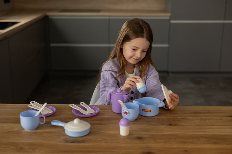 A young girl enjoys playtime with colorful toy tableware in a modern kitchen setting.