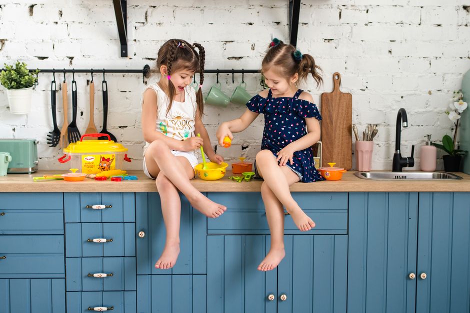 Two girls enjoying playtime with toy kitchen set on a blue counter indoors.