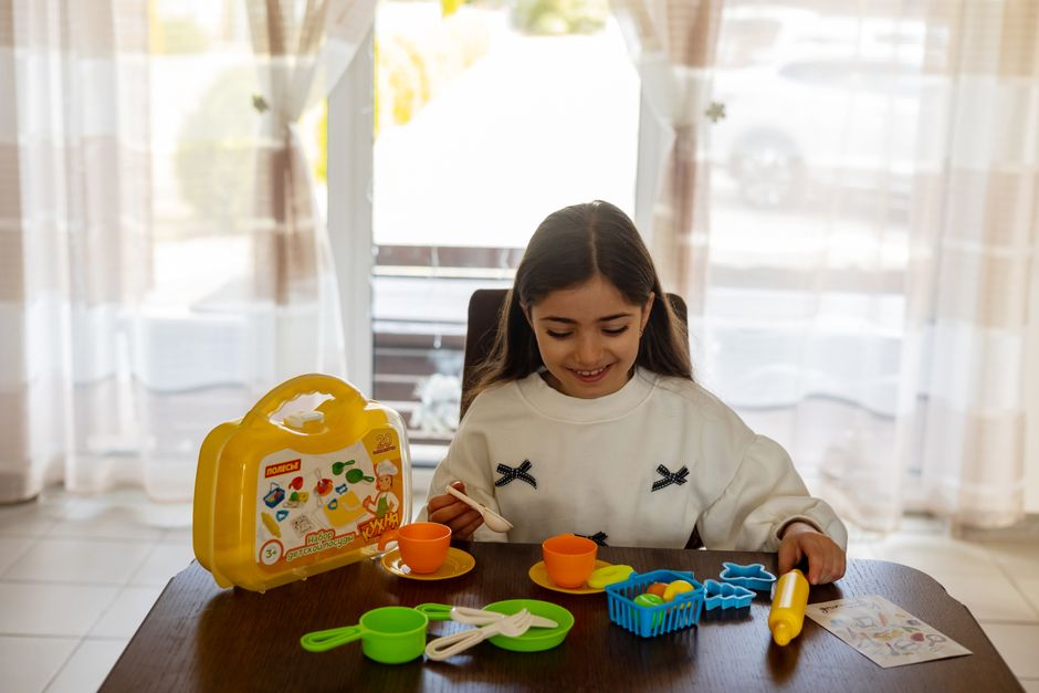 A young girl happily plays indoors with a colorful toy kitchen set.