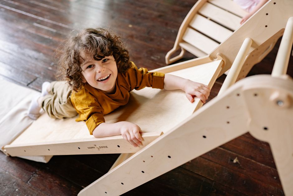 Smiling child playing on a wooden slide indoors, embracing fun and joy.