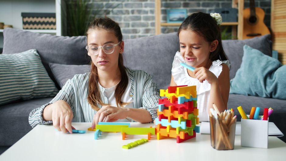 Two sisters playing with colorful blocks indoors, fostering creativity and learning.