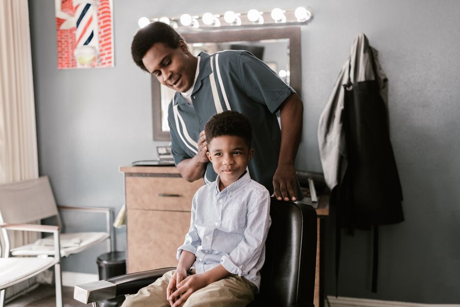 Smiling boy receives a haircut from a barber in a stylish barbershop setting.