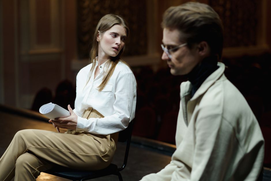 Two actors in a theater setting deeply engaged in a script rehearsal scene.