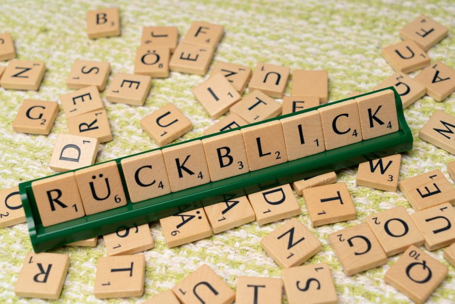 Wooden Scrabble tiles arranged to spell 'Rückblick' on a textured surface, showcasing language and typography.
