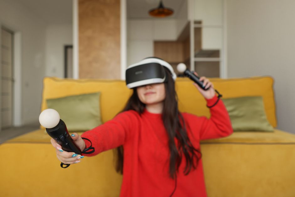 Woman in red shirt using VR headset and controllers for gaming indoors.