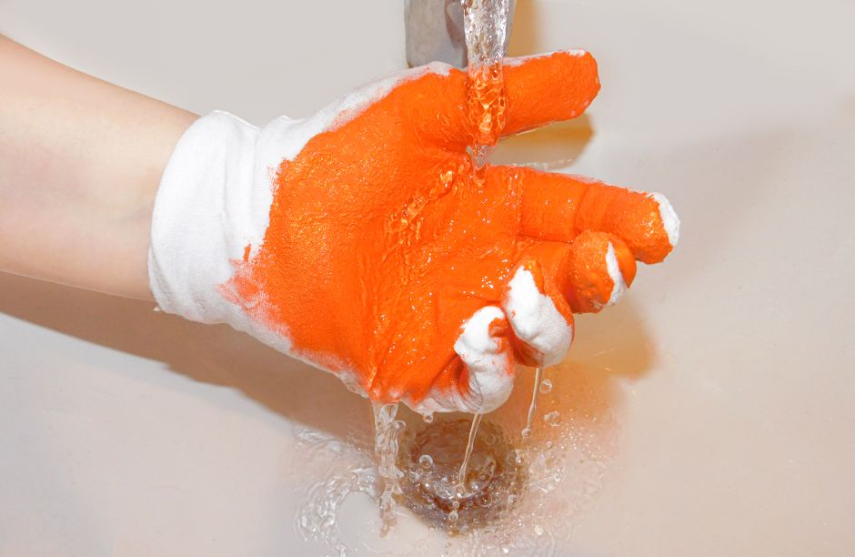 Orange-coated gloved hand under running water, capturing splash and texture.