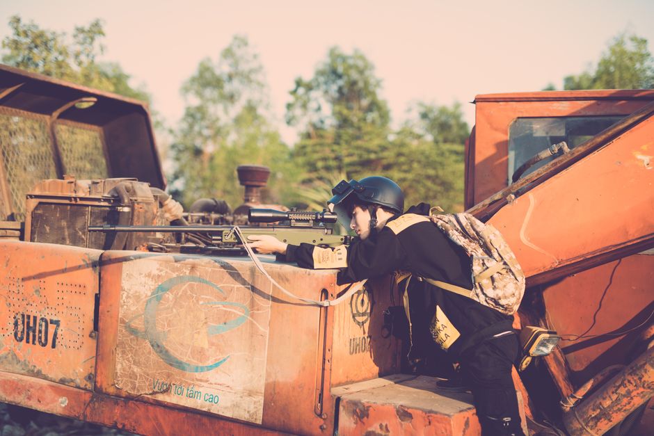 Person engaging in realistic outdoor play with a toy sniper rifle on industrial machinery.