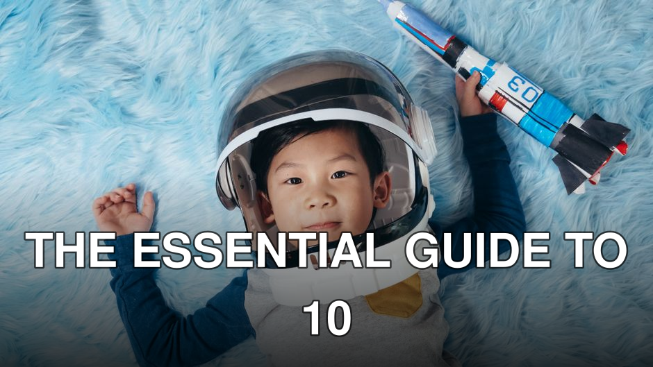 Cute young boy wearing astronaut helmet, lying on blue carpet, holding toy rocket.